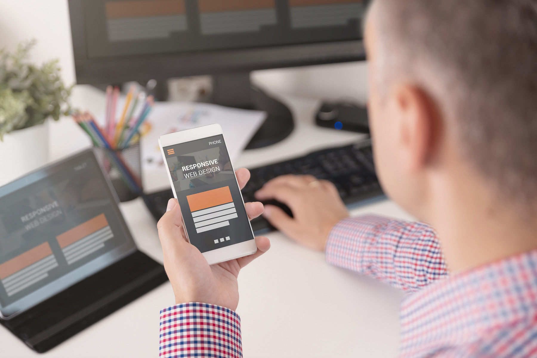 Man looking at mobile phone and laptop while typing - iStock-1038490818.jpg